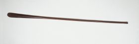 Long oar-shaped club made of hard black wood, with a round shaft becoming a flat blade ending in a curve.
