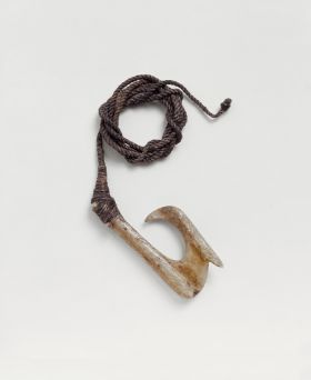 Fishhook made of bone with a straight shank. A barb is located on the outer side of hook, directly below the point. A brown fishing line is attached to the hook.