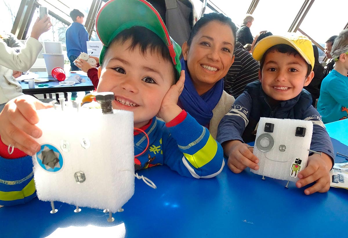 Colour photograph of a woman posing with two children displaying hand-made craft objects.