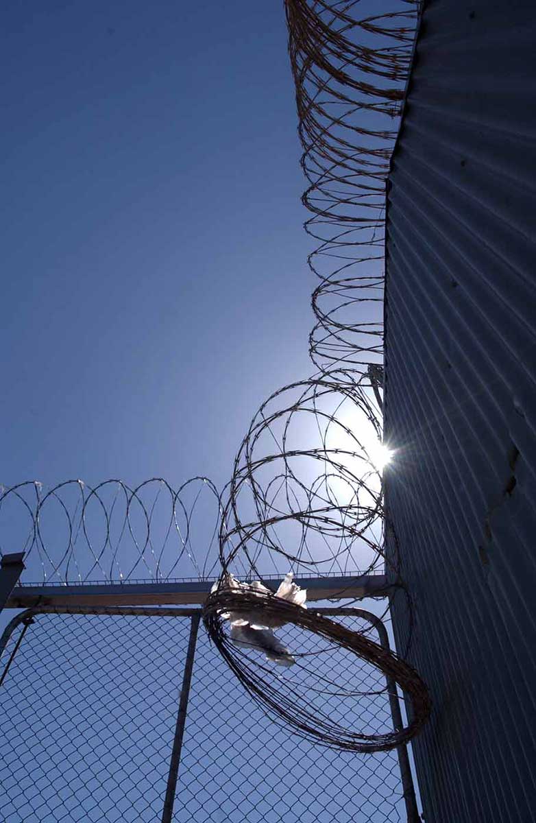 Photo looking into the sun at the top of a gate with barbed wire on top - click to view larger image