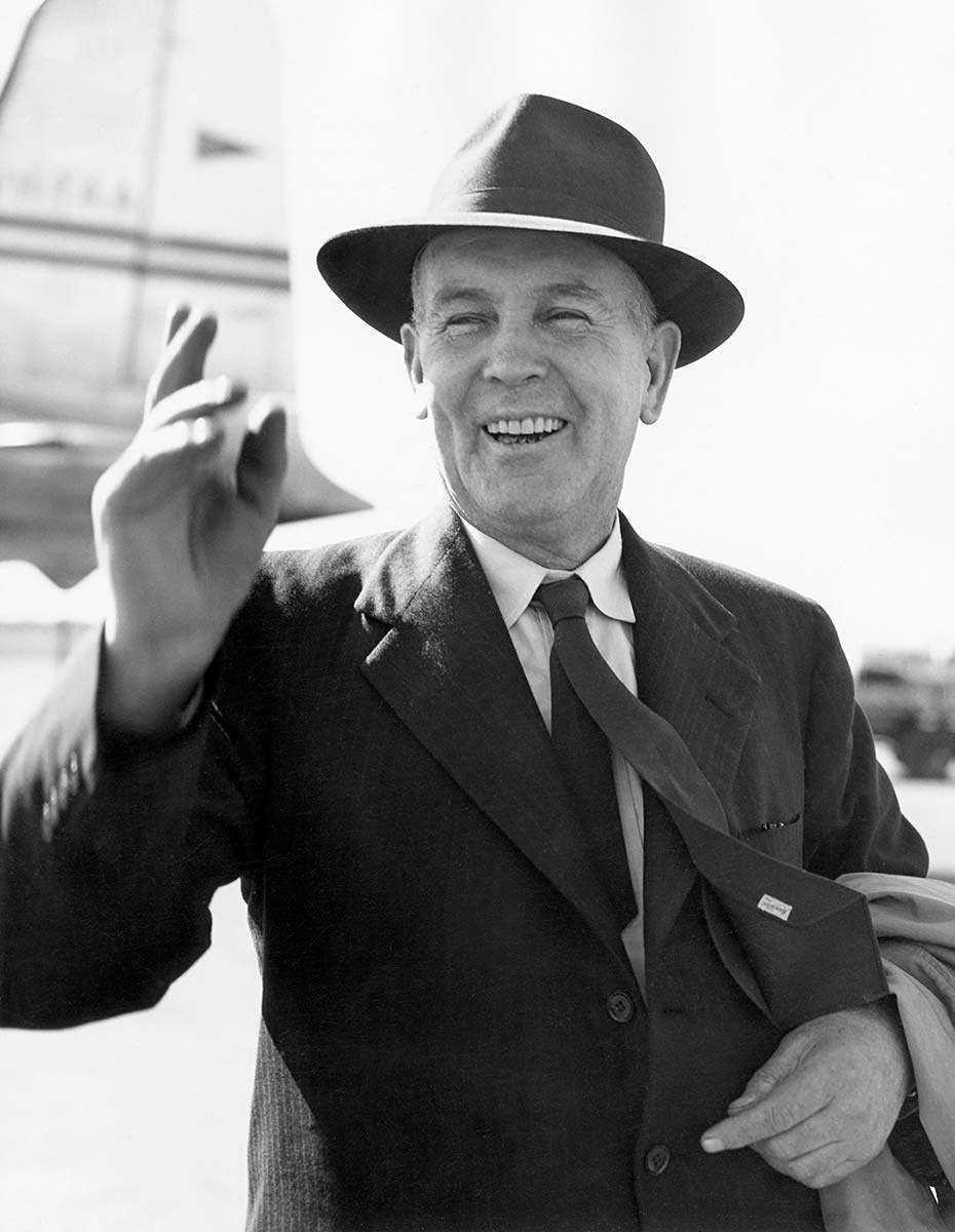 Chifley on the tarmac of an airport, smiling and waving. - click to view larger image