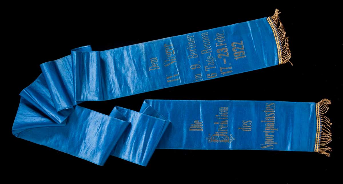 Blue textile sash with dark gold fringed ends and German text. - click to view larger image
