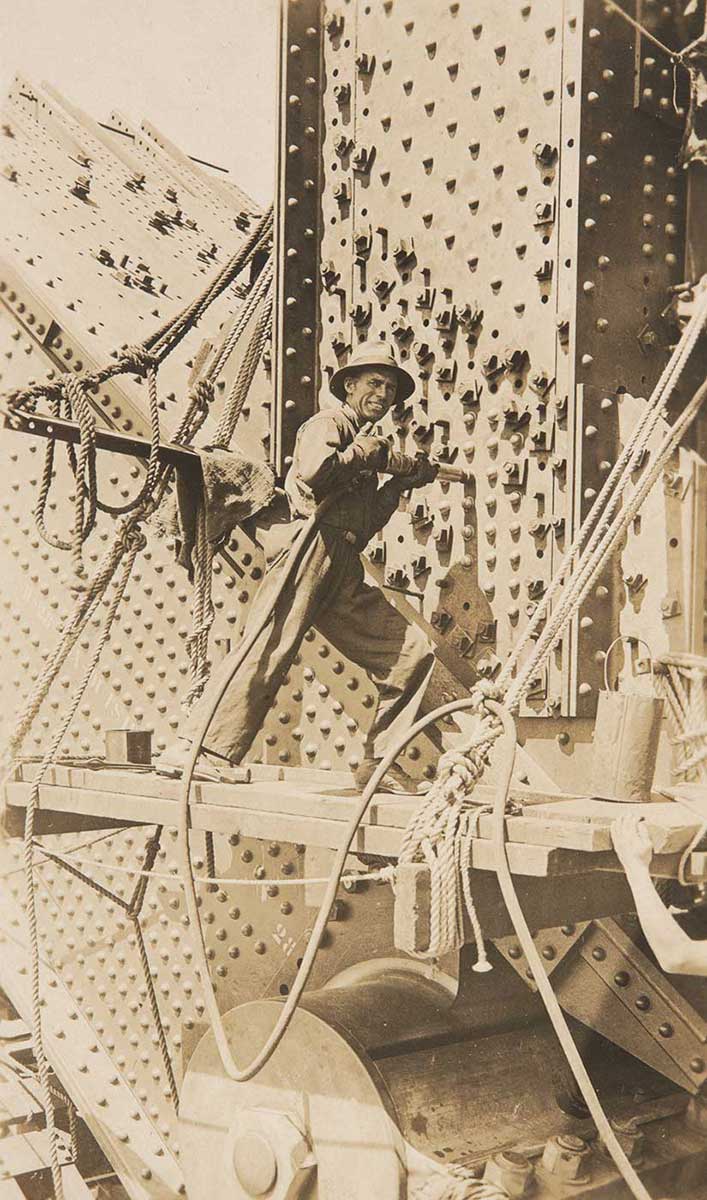 A man using a hand-held rivet gun during the construction of the Sydney Harbour Bridge. - click to view larger image