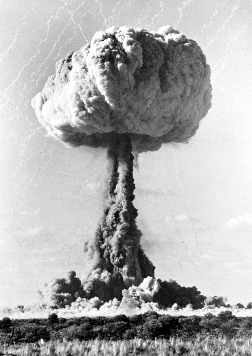 classic mushroom cloud of a nuclear explosion in the background, with grassy scrub in foreground - click to view larger image
