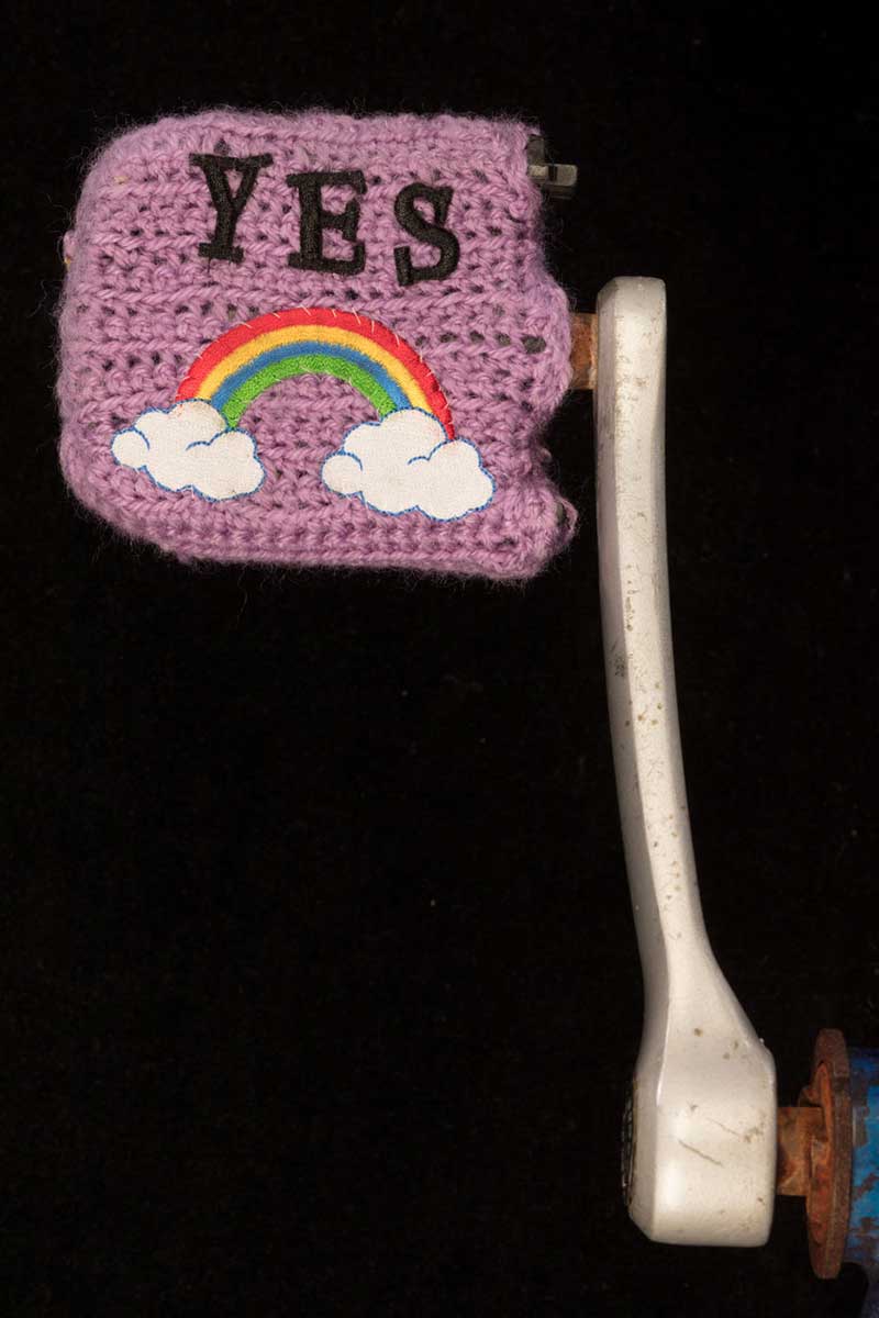 Pedal covered in mauve wool with the word 'YES' above a rainbow ending in clouds. - click to view larger image