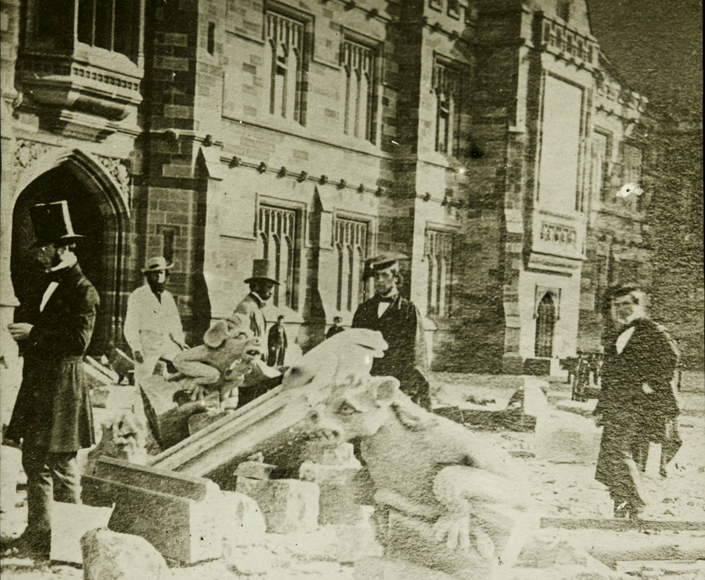 Faded black and white photograph of men amongst rubble, in front of a sandstone building. - click to view larger image