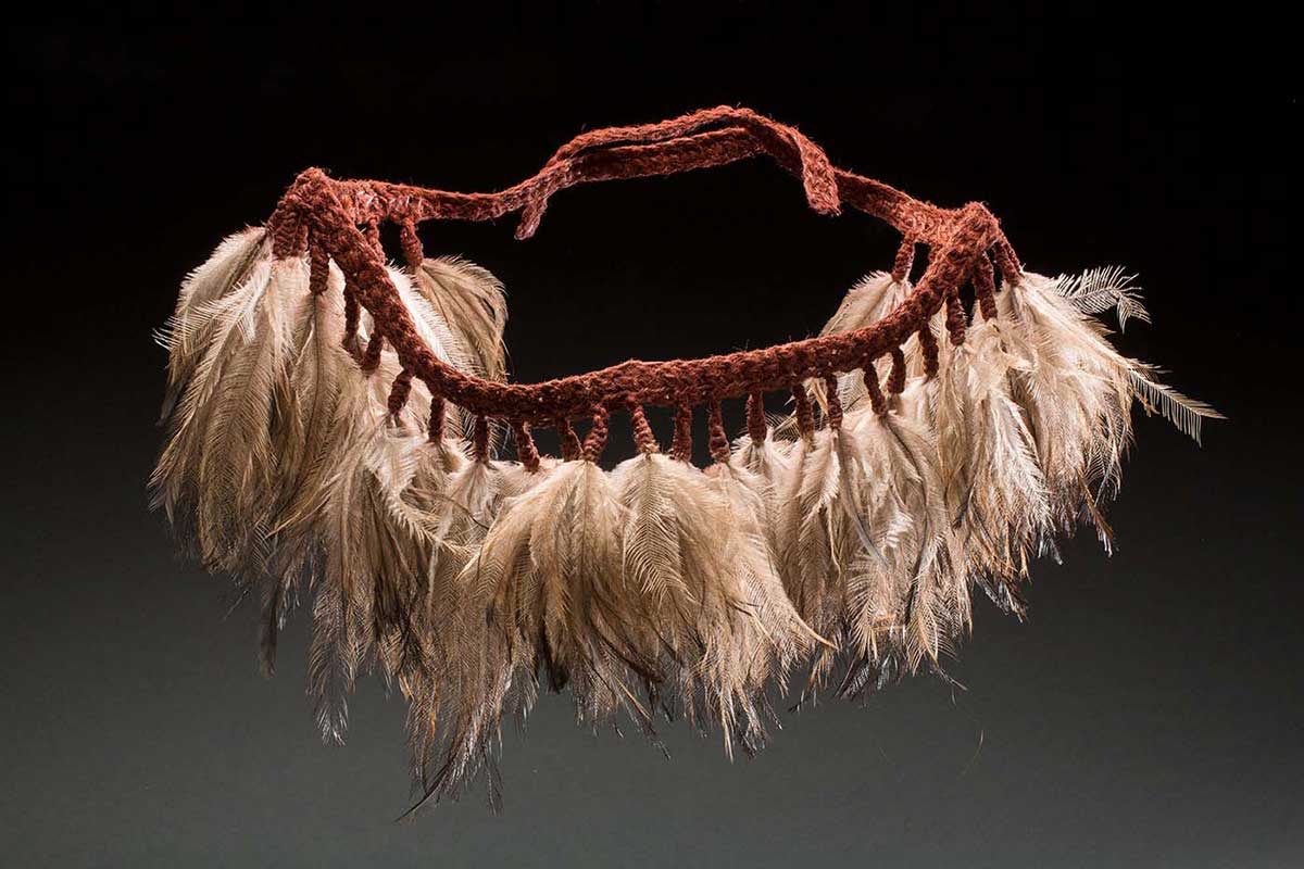 A skirt with a woven fibre belt that is pigmented with a red ochre colour. Every couple of centimetres along the belt hangs a group of emu feathers held in place by woven fibre. There are 34 groups of feathers with some of the woven fibre belt at either end of the skirt so it can be tied on. - click to view larger image