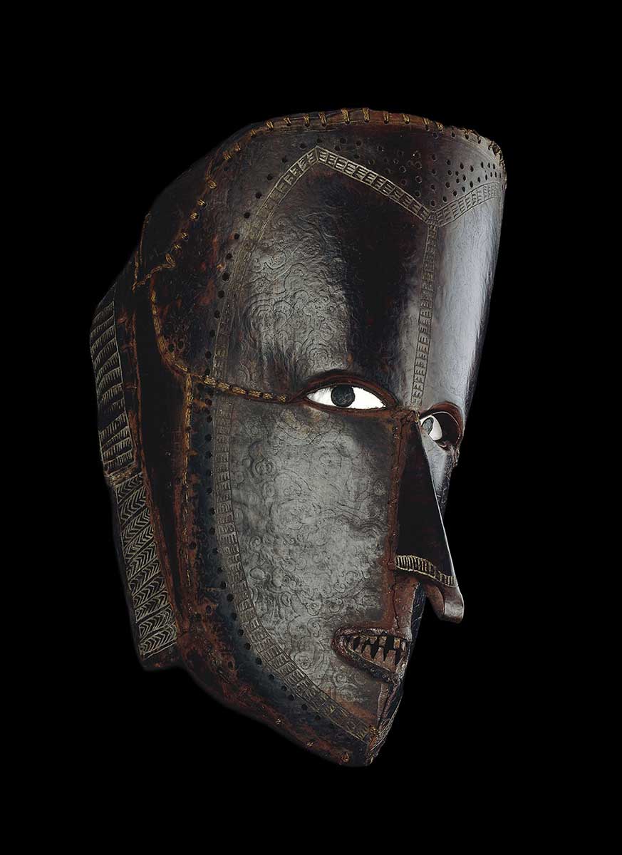 Mask made of tortoise-shell plates which have been bent to form an elaborate human face, and sewn into place with fibre; shell eyes. - click to view larger image