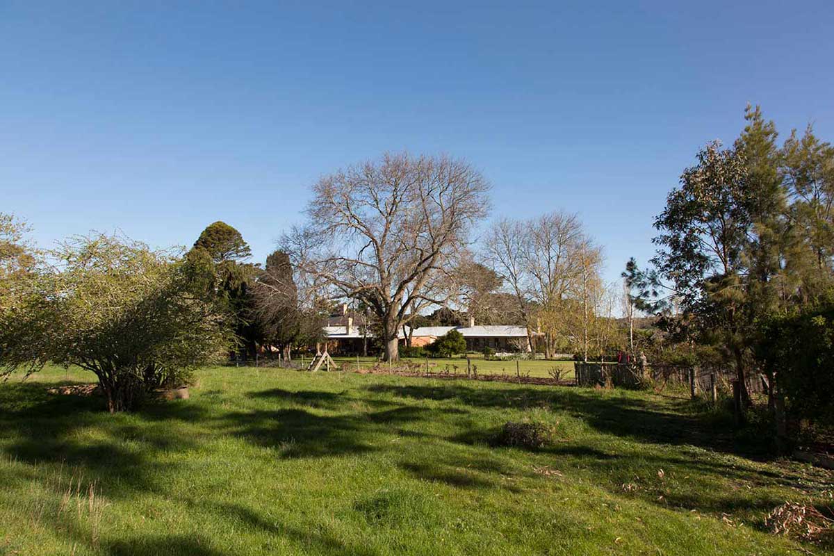 Country setting featuring a house with a tin roof surrounded by grass, trees and garden.