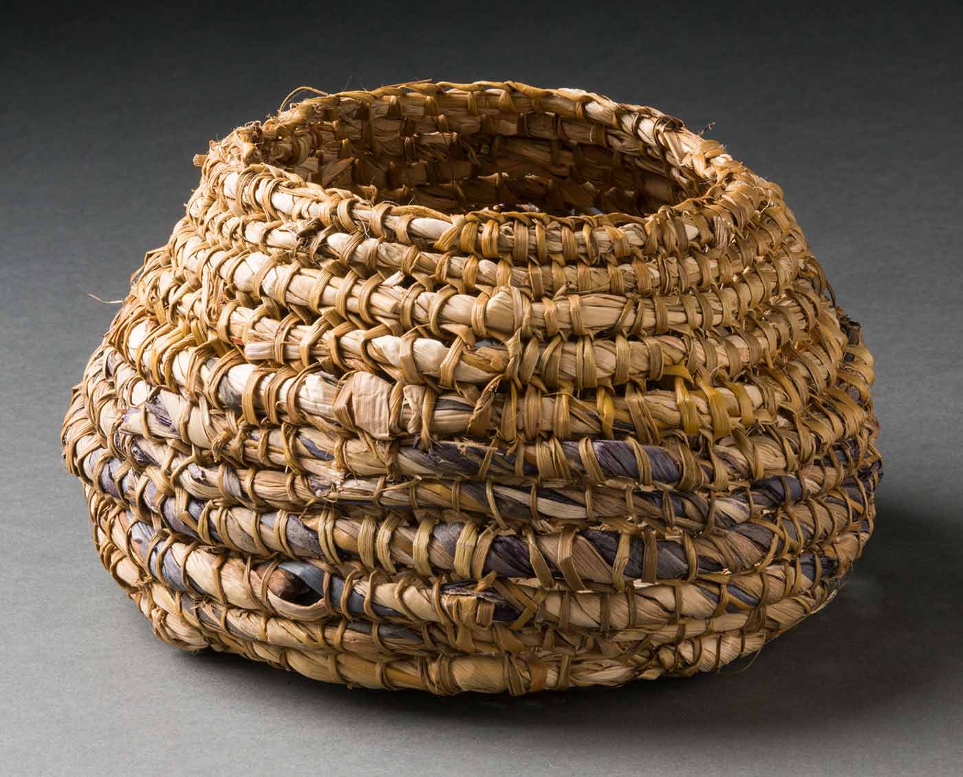 A circular coiled basket with a flat base and convex sides that taper towards the top to a smaller circular opening.