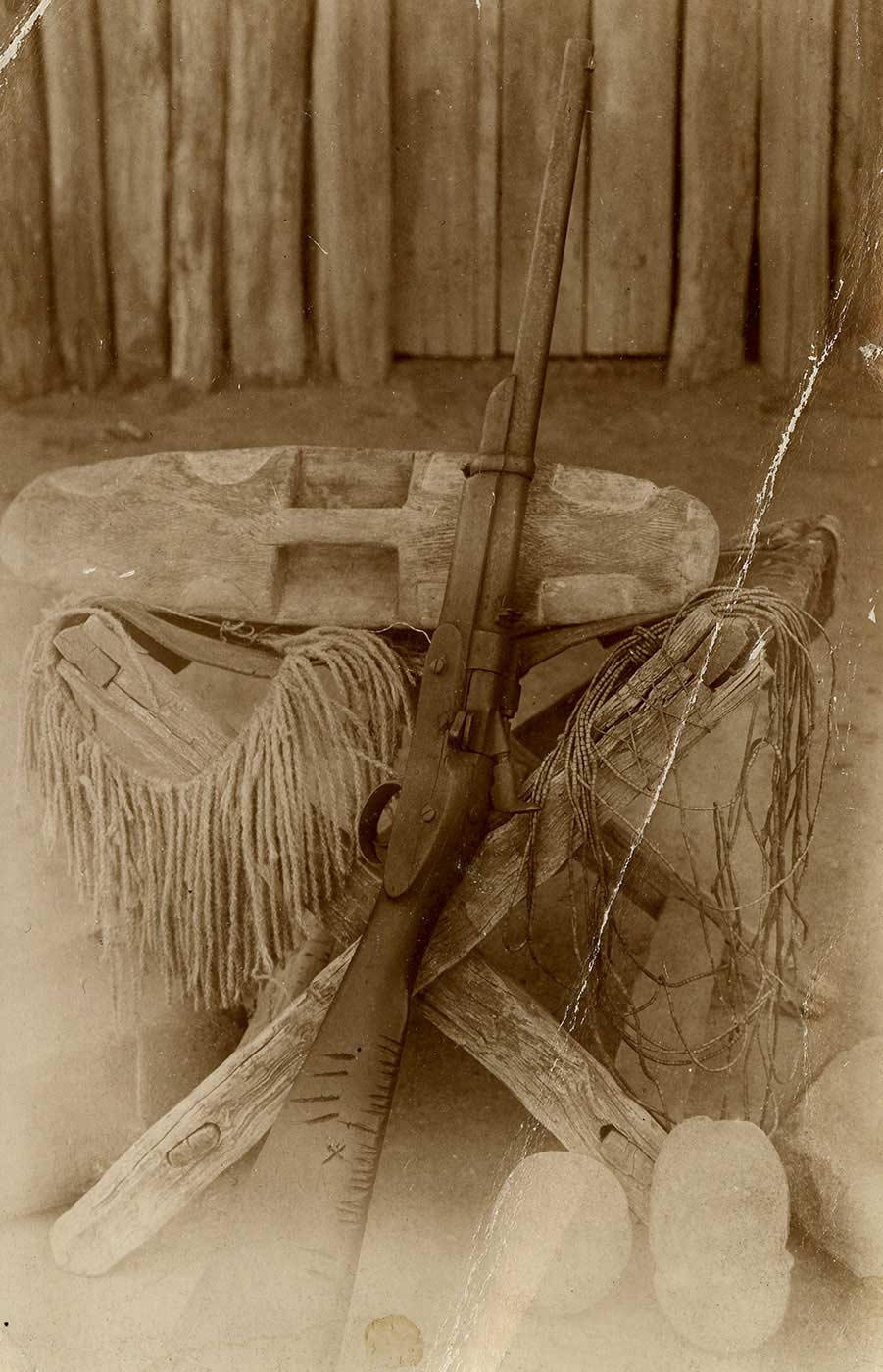 An old postcard of a gun resting against a stool with a wooden shield on top. - click to view larger image