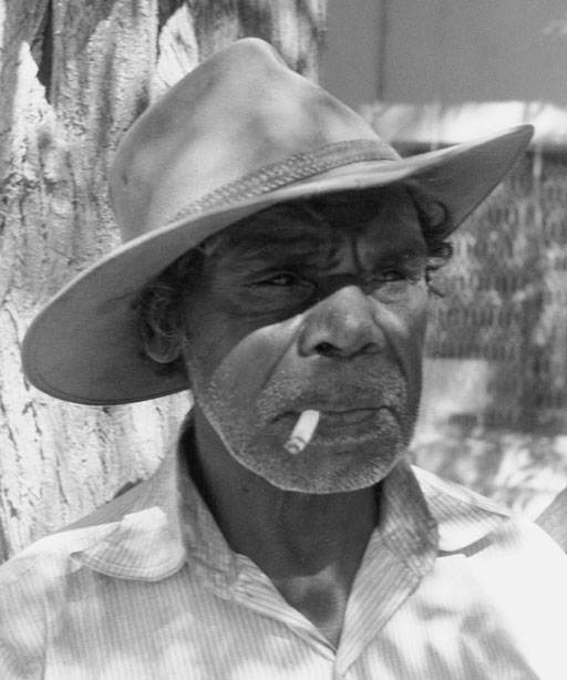 Portrait photo of an Aboriginal Australian man wearing a hat and smoking a cigarette. - click to view larger image