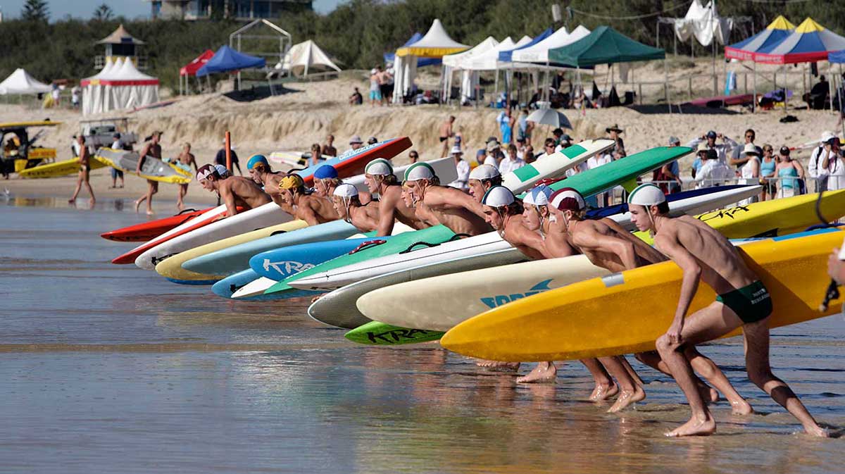 Surf lifesavers on the beach with their boards poised at the start line of a race.