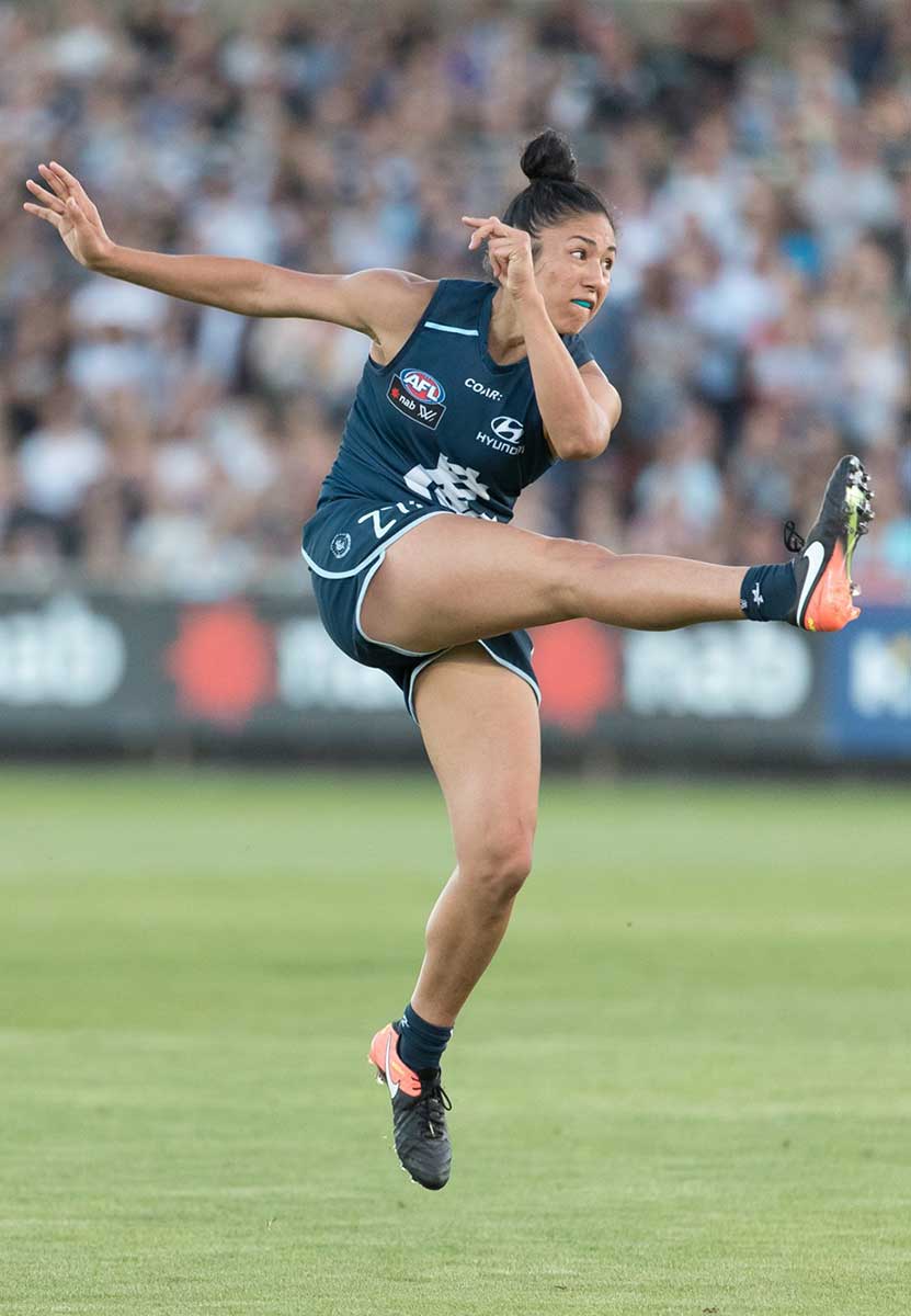 A photograph of Darcy Vescio in mid-air after she kicks the football. - click to view larger image