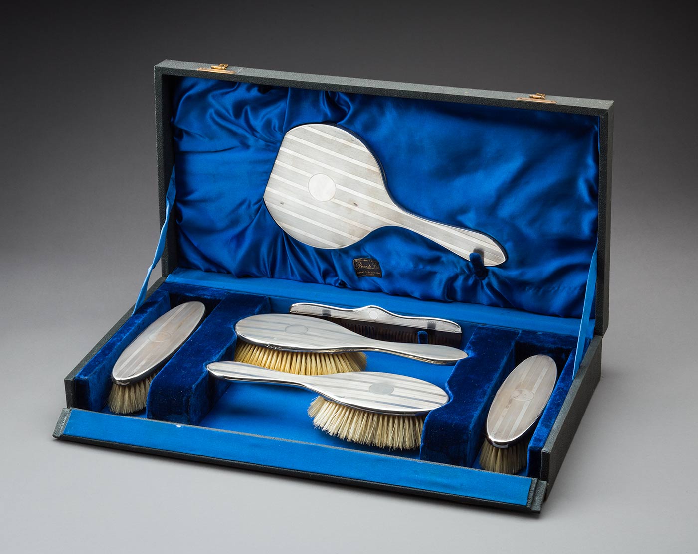 Blue velvet lined dressing case holding two hair brushes, two clothes brushes, a comb and a mirror.