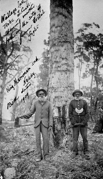 Black and white photograph of two men in front of a marked tree. There is hand written text on the photo including: King Merryman and Neddy. Both dead. 1909.