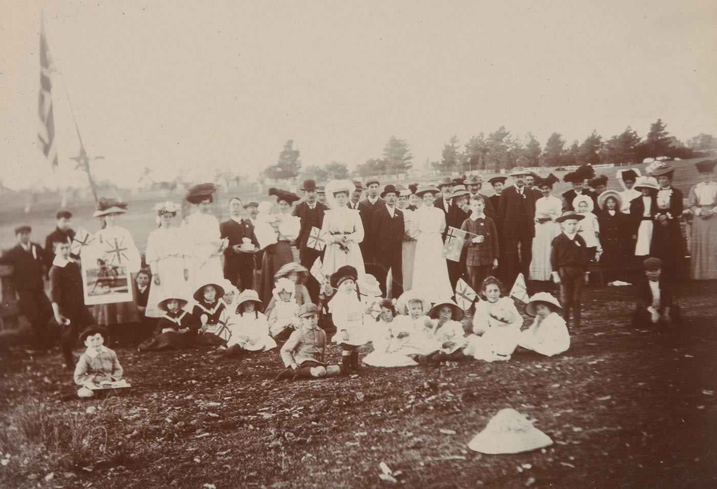 Black and white photo showing a group of people including many children at front. Some of the crowd holds flags. - click to view larger image