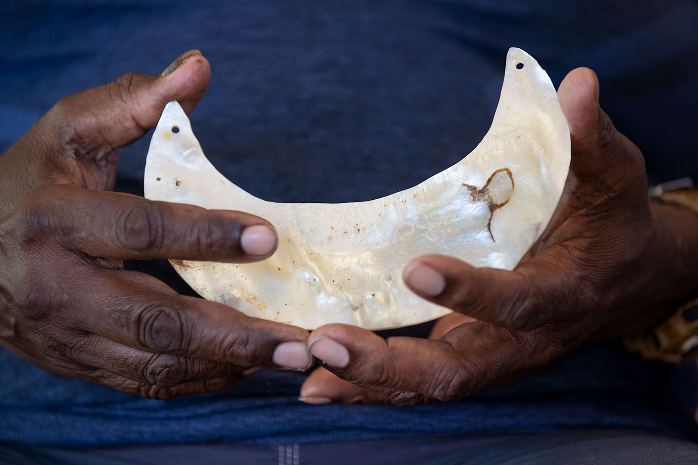 Colour photo of two hands holding a shell in the shape of a crescent.