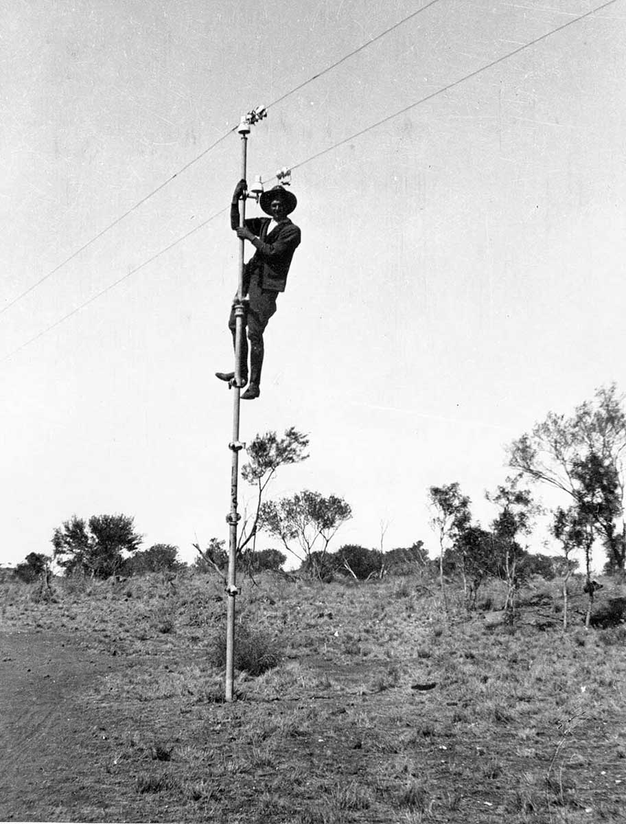 A black and white photo taken in the 1920s of a man who has climbed up to the top of a pole. - click to view larger image