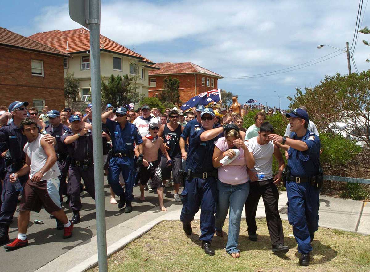Young people being protected by police from a riot of predominantly white male protesters with the Australian flag.