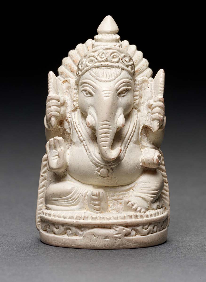 Intricately carved statue of a seated mythological figure which features the head of an elephant and the body of a man. The figure has multiple arms which are in a series of poses or holding objects. - click to view larger image