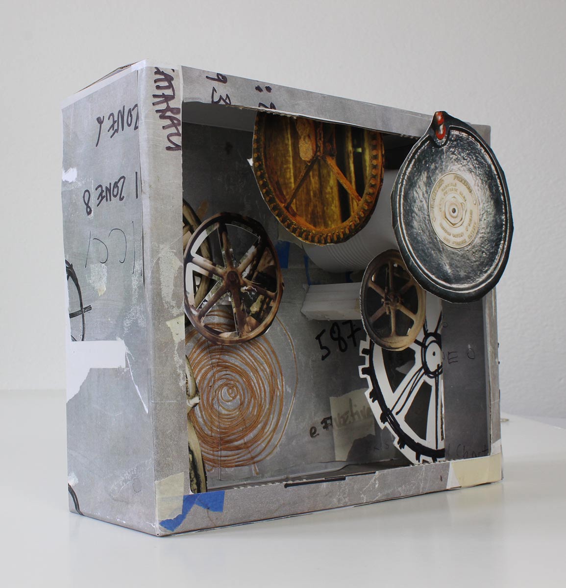 Diorama constructed from cardboard and various other materials. The interior of the box features cut-out colour images of round mechanical objects. - click to view larger image