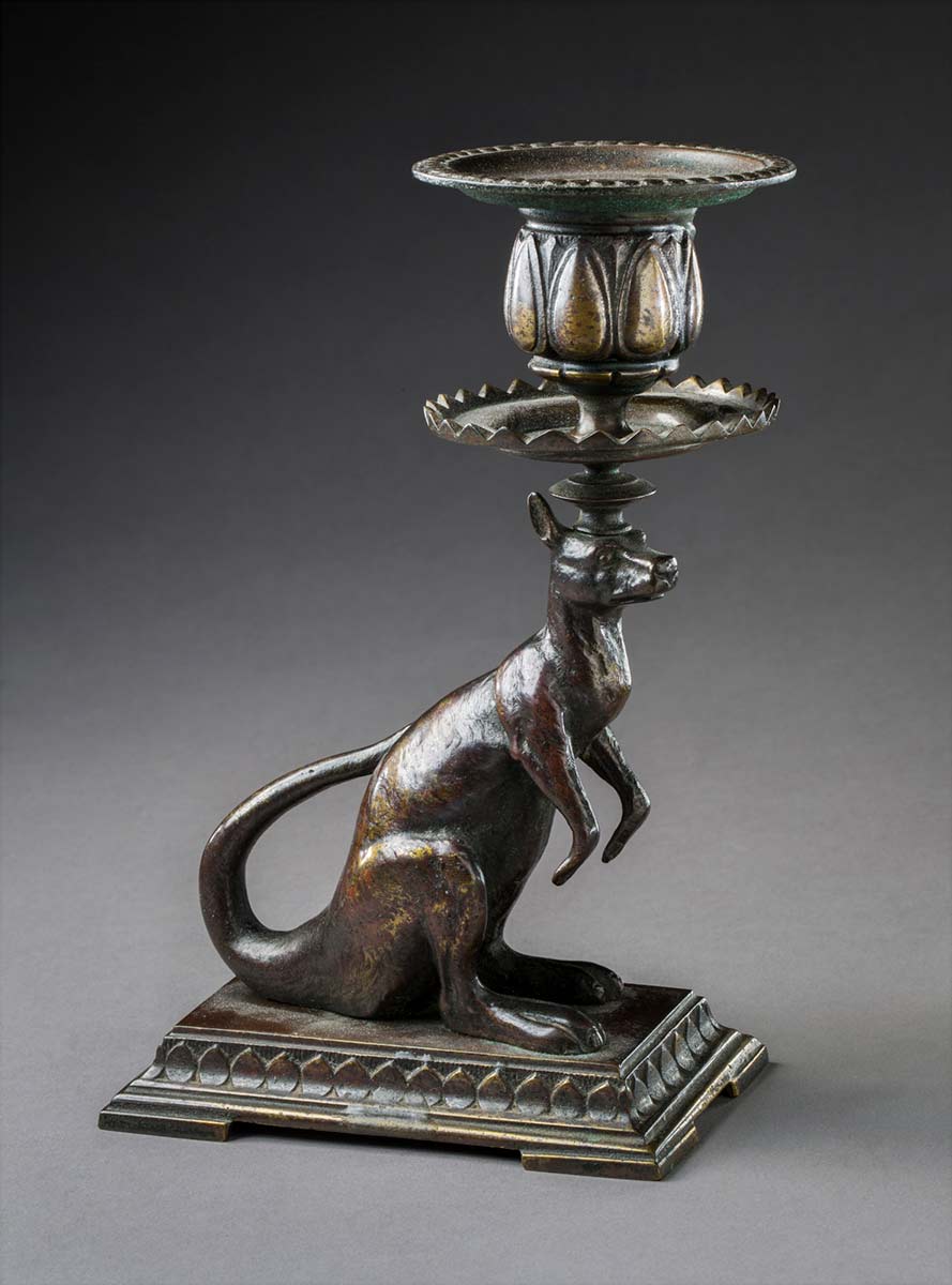 A cast kangaroo candlestick mounted on a rectangular plinth. The candle nozzle and pan are mounted on the kangaroo's head. - click to view larger image
