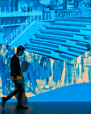 Side view of a man walking in front of an image projected on to a wall in shades of blue and yellow. - click to view larger image