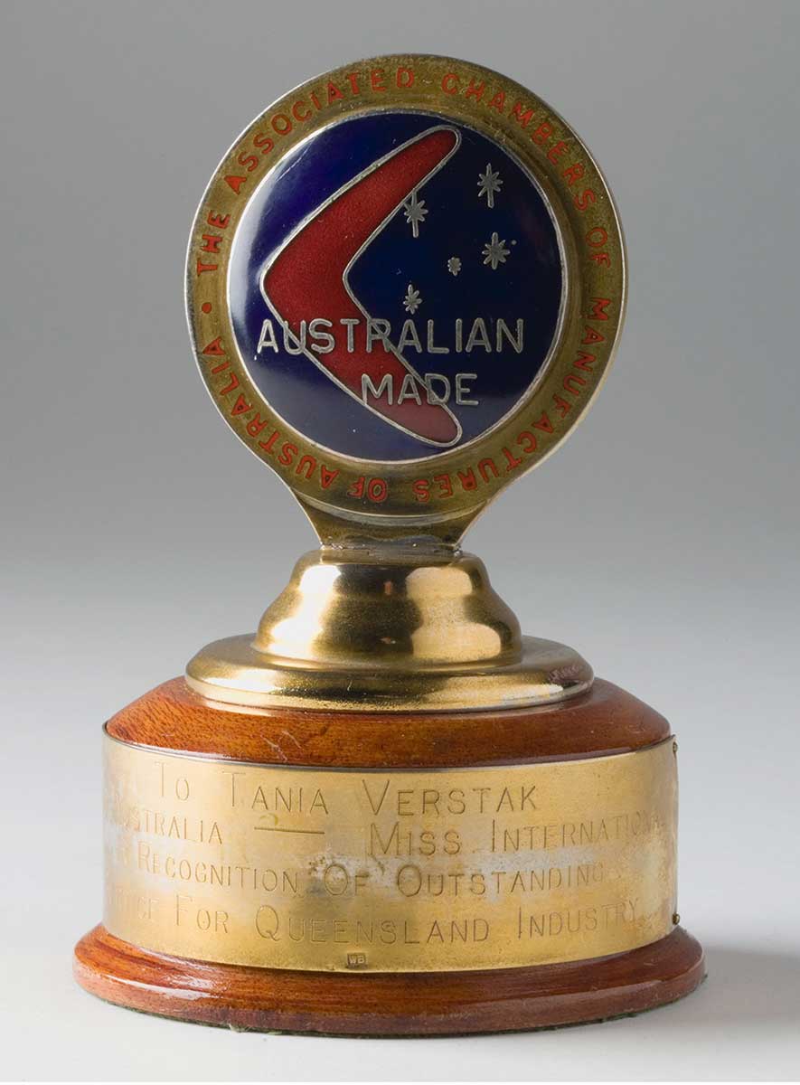 Trophy with a circular wooden base, topped with by a metal disc with 'Australian Made' written on it and an image of a boomerang and the five stars of the Southern Cross. A gold-coloured plate on the base reads: 'To Tania Verstak, Miss Australia-Miss International, in recognition of outstanding service for Queensland industry'. - click to view larger image