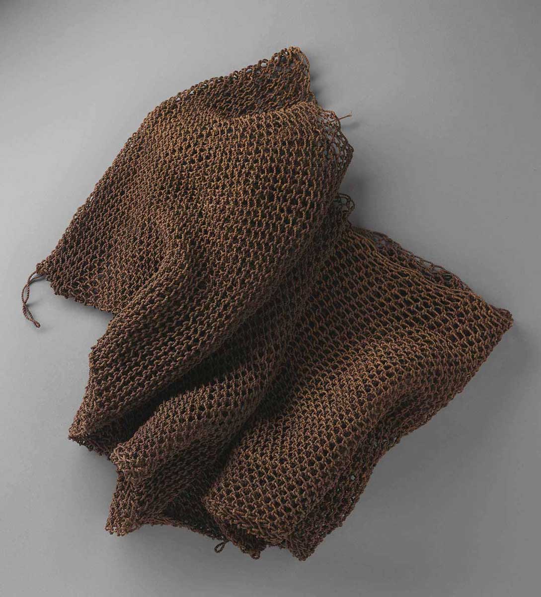 A fishing net, made from natural fibre string. The net is folded in upon itself, suggesting that it is larger than it looks. The string is light brown in colour; the precision of the weaving indicates that it was made by a skilled First Nations weaver. - click to view larger image