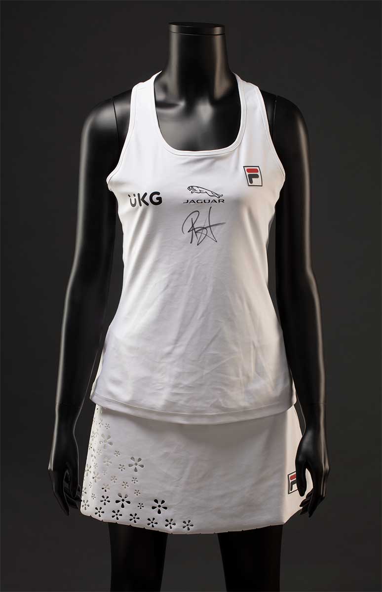A white Fila 'Trailblazer' tennis outfit consisting of a tank top and skort. The front features a 'UKG' logo and 'JAGUAR' logo, as well as a handwritten signature in black ink. The skort has a laser cut scalloped hem and floral decoration at the front and side. - click to view larger image