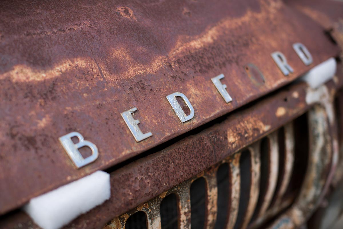 Detail of a rusty car bonnet. Metal letters spelling out 'BEDFORD' are fixed to the front although the 'O' is missing. - click to view larger image