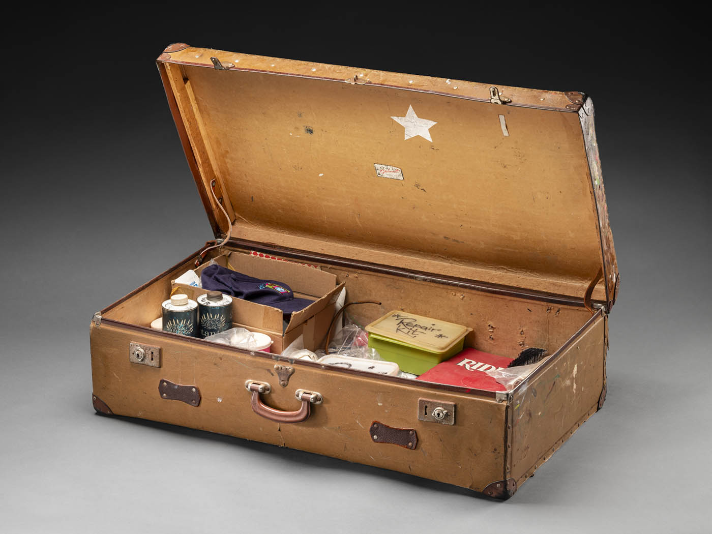A photograph of Norman Hetherington’s suitcase which he took to the studio when recording. The suitcase is brown with a leather handle and two lockable metal latches.
