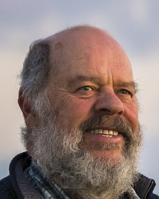 A photograph of Denis Rose. He is smiling and has a beard.