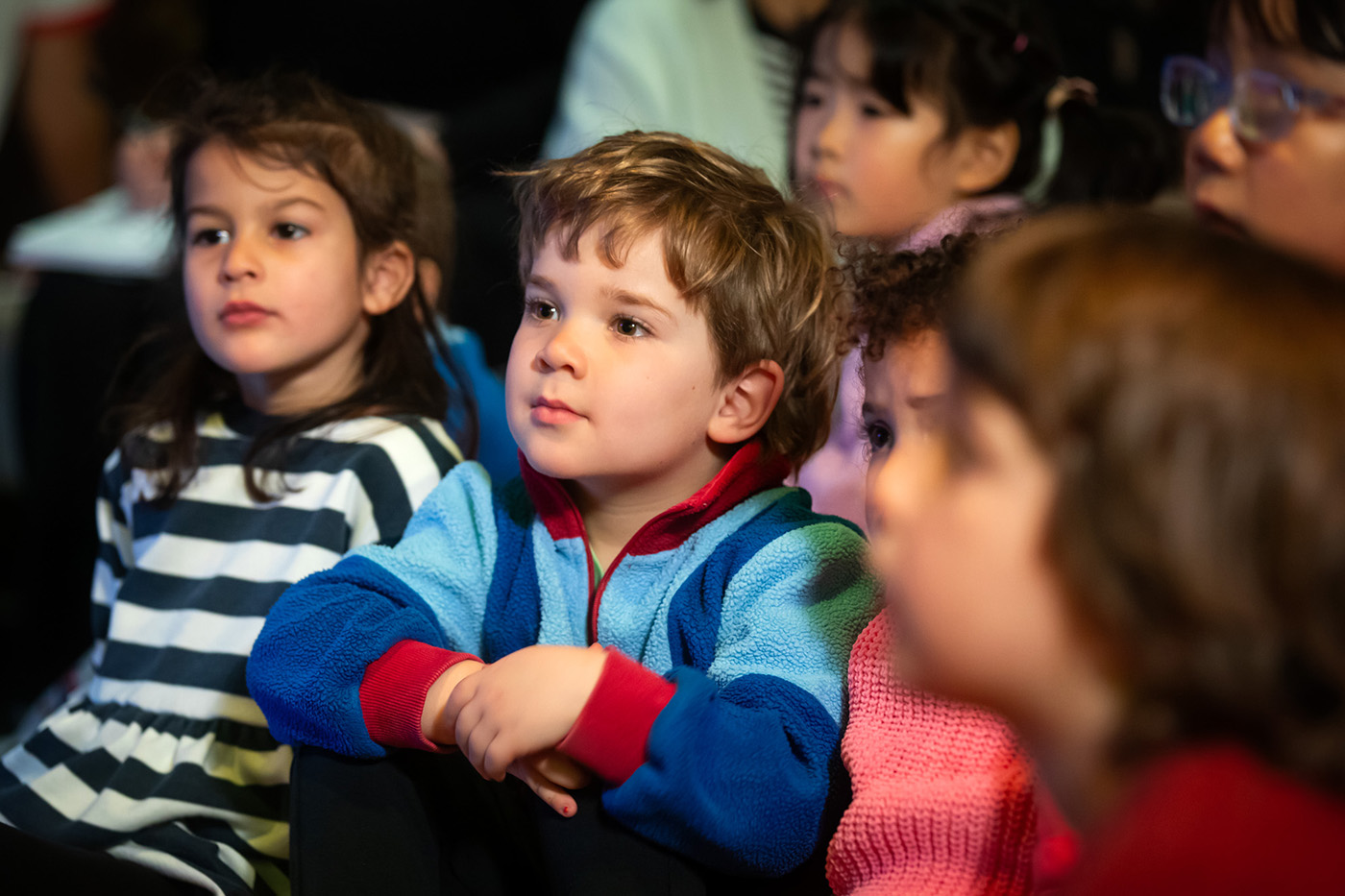  A group of young children, sitting on the floor, captivated.