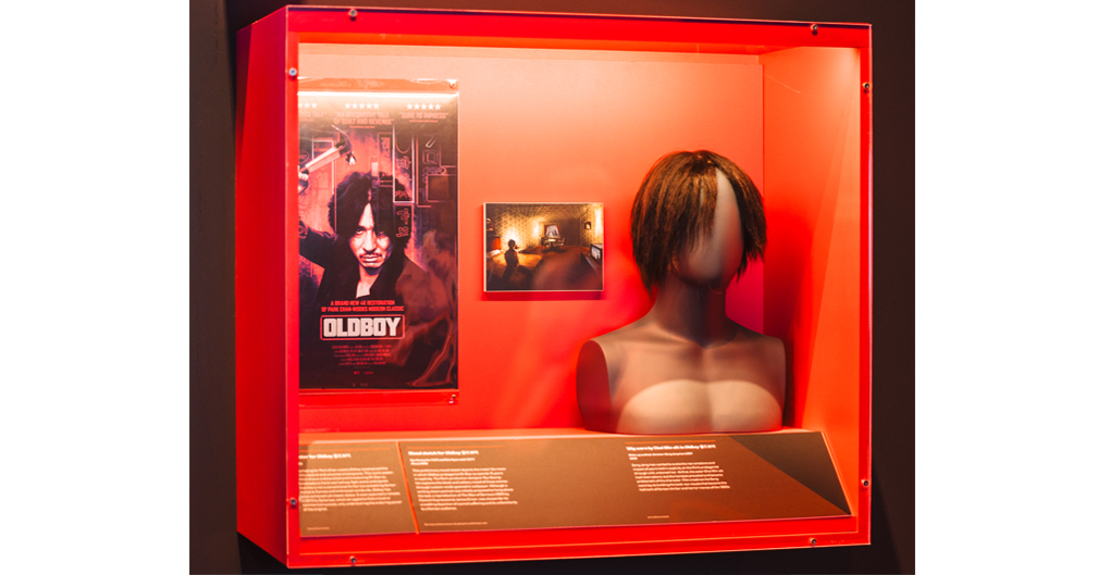 A black torso features a wig on the head. The wig is characterised by a central part and straight, longish hair, which is shaggy and falls below the ears but above the shoulders. The overgrown, unkempt style falls straight over the face and over the ears of the mannequin head.