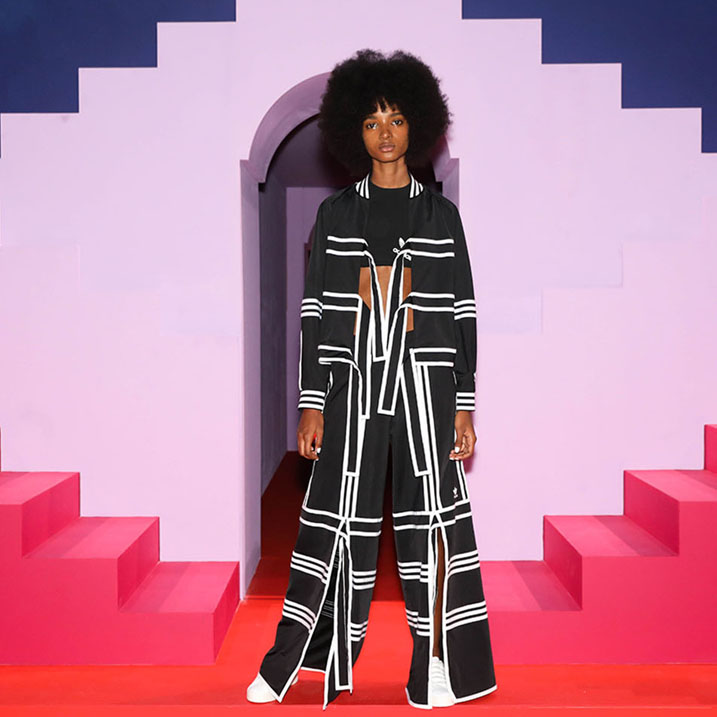 A photo of a model in a black and white Korean inspired adidas tracksuit. Behind the model is a backdrop with purple, pink, red and navy steps creating a geometric backdrop.