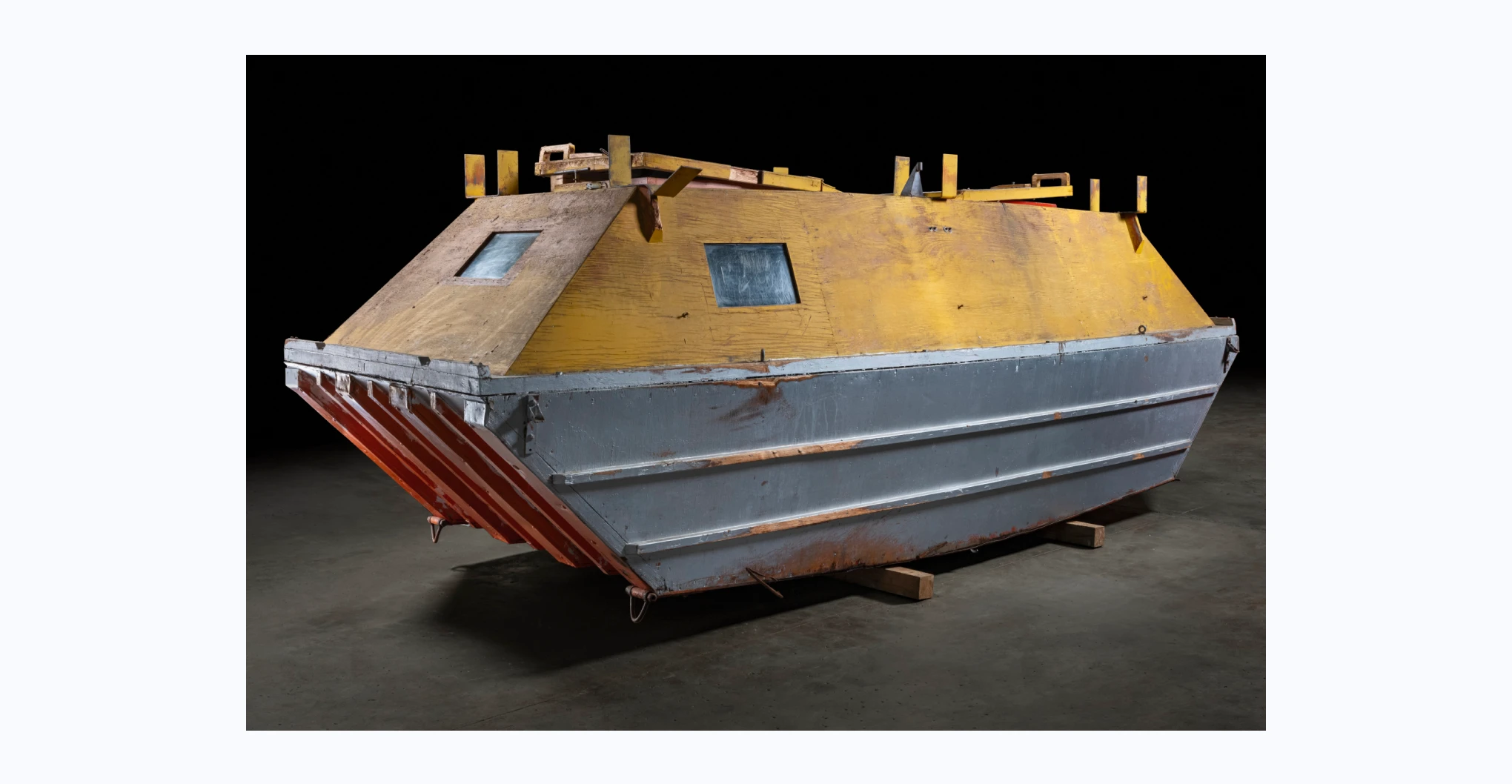 The barge caravan consists of trapezoid shaped top and bottom sections bolted together with ferrous nails and bolts. The top is painted yellow and the bottom orange and silver. The bottom is constructed from plywood and has a slightly curved base and sides with four metal capped hardwood runners running from front to back with three uncapped runners between. Along each side of this section are two rubbing strips.