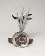 Headband made of coconut fibres, interwoven, and attached to a round plate of Mother-of-pearl where long black and white tail feathers protrude behind it.