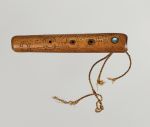 Flute made of light brown wood, embellished with spiral patterns in dots and lines, with a mother-of-pearl plate and three holes, at one end with the remains of a twisted cord.