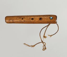 Flute made of light brown wood, embellished with spiral patterns in dots and lines, with a mother-of-pearl plate and three holes, at one end with the remains of a twisted cord.