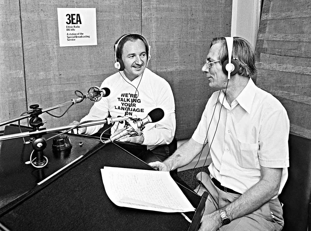 Two men sitting in a radio studio in front of microphones. They are smiling and clearly in conversation. The present is wearing a top saying ‘We’re talking your language on 3EA’.