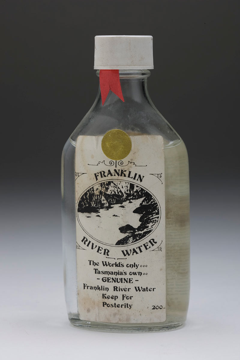 studio shot of bottle of water with a dirty label reading Franklin River water. The world’s only. Tasmania’s own. Genuine Franklin River Water. Keep for posterity. 200 ml