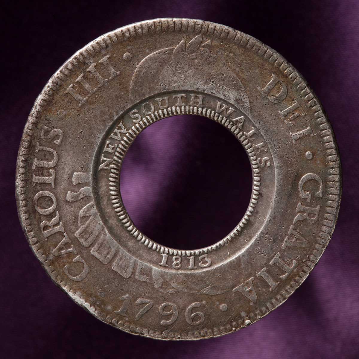studio photo of silver coin with missing centre. The original Spanish imprinting in Latin is visible around the outside rim, while the words five shillings have been imprinted around the inside rim