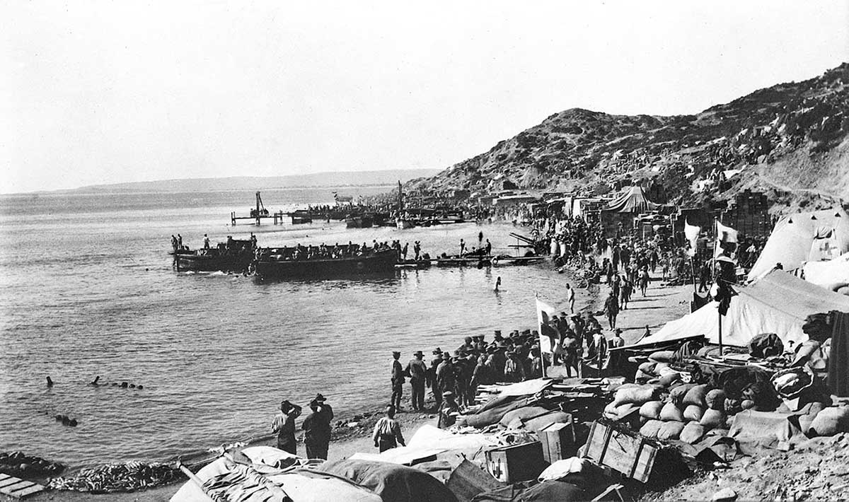 Slightly damaged black and white photo of soldiers on a narrow beach with steep escarpment behind them.