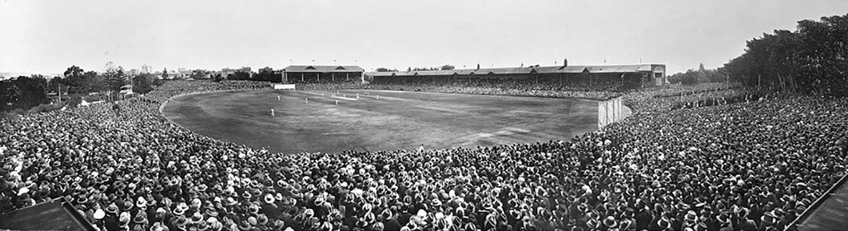 Black and white photograph of a cricket match being viewed by a large crowd of spectators.