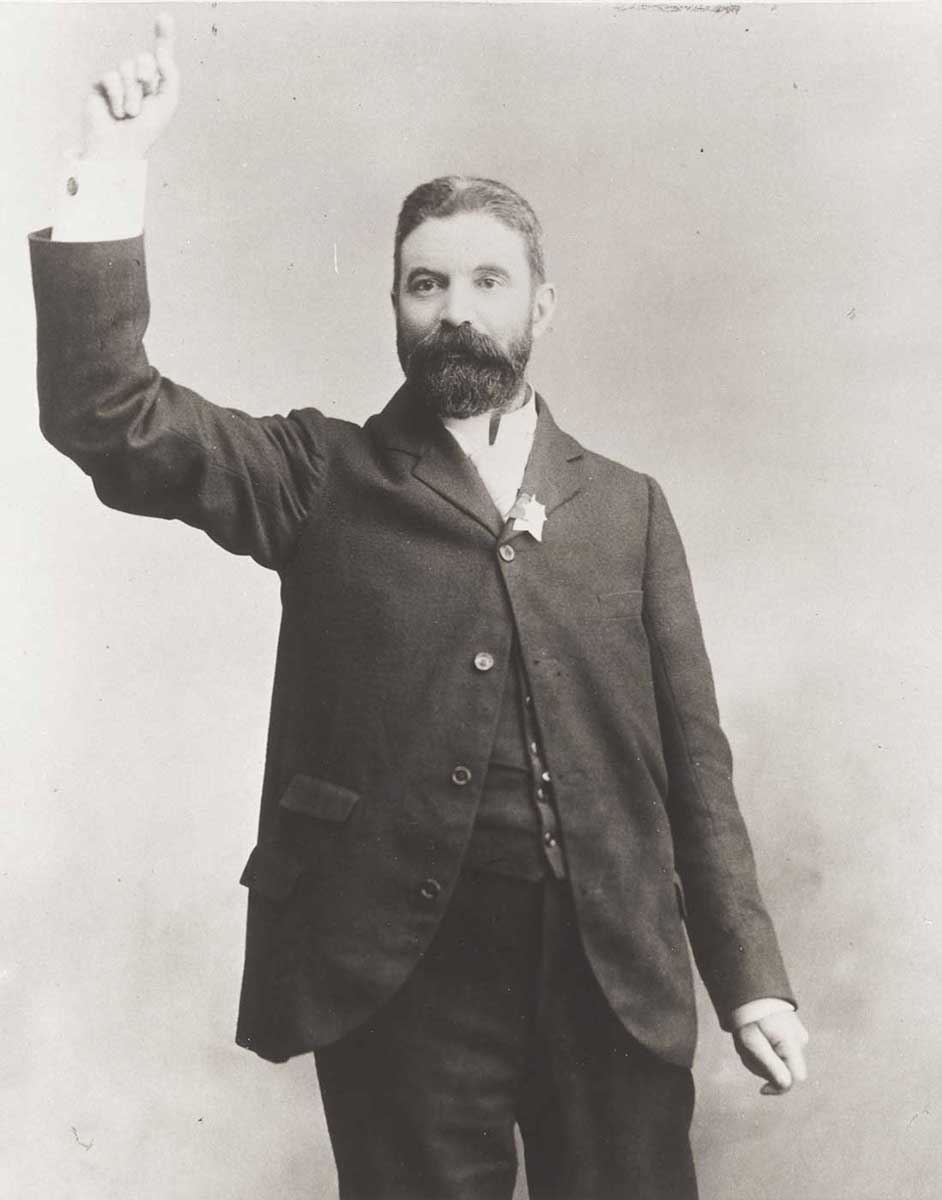 Black and white photo of man with dark beard posing as though he is addressing a crowd. - click to view larger image