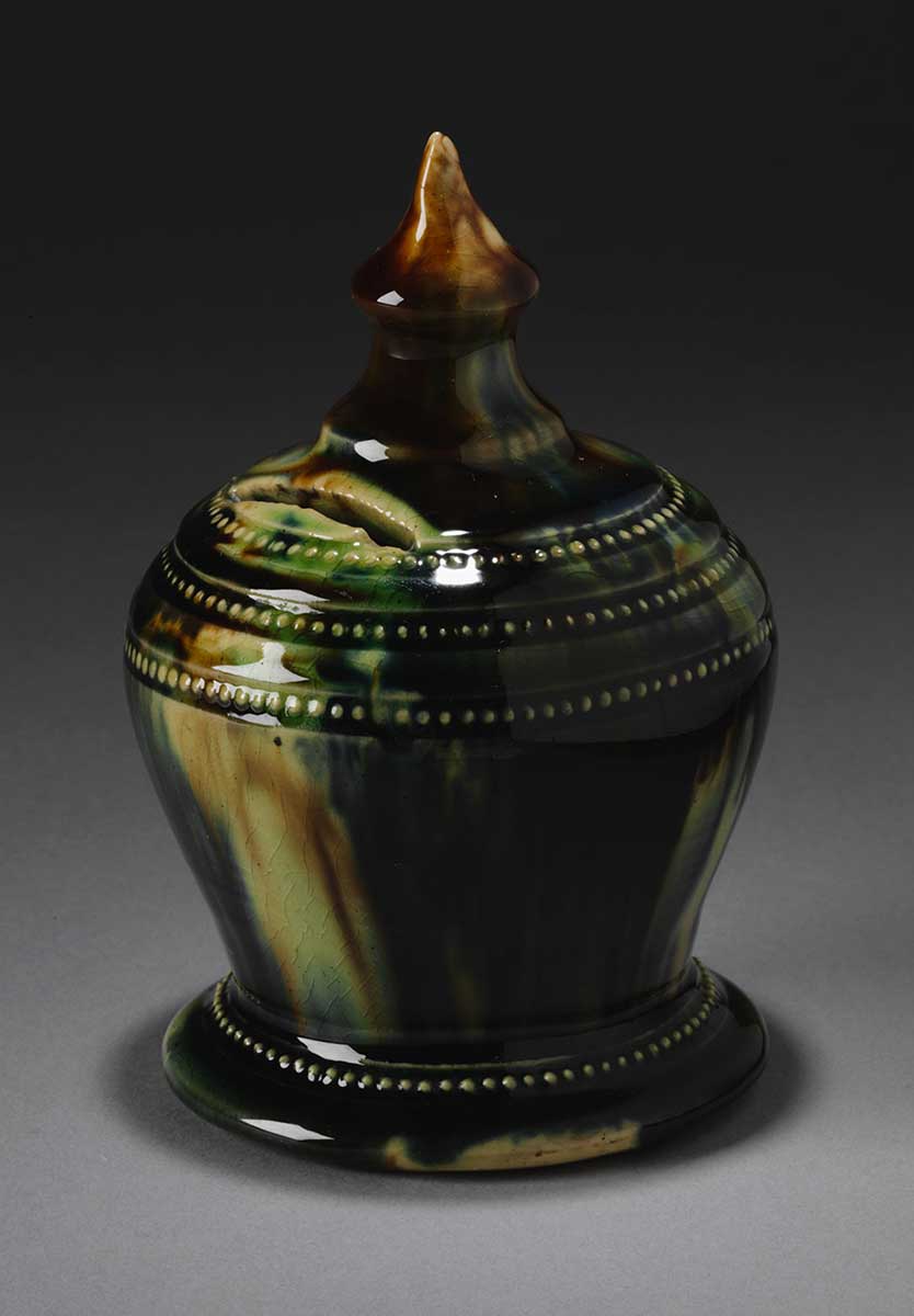 Dark green glazed, vase shaped ceramic money box with a circular base and spherical middle, tapering to a cone-shaped knob. - click to view larger image