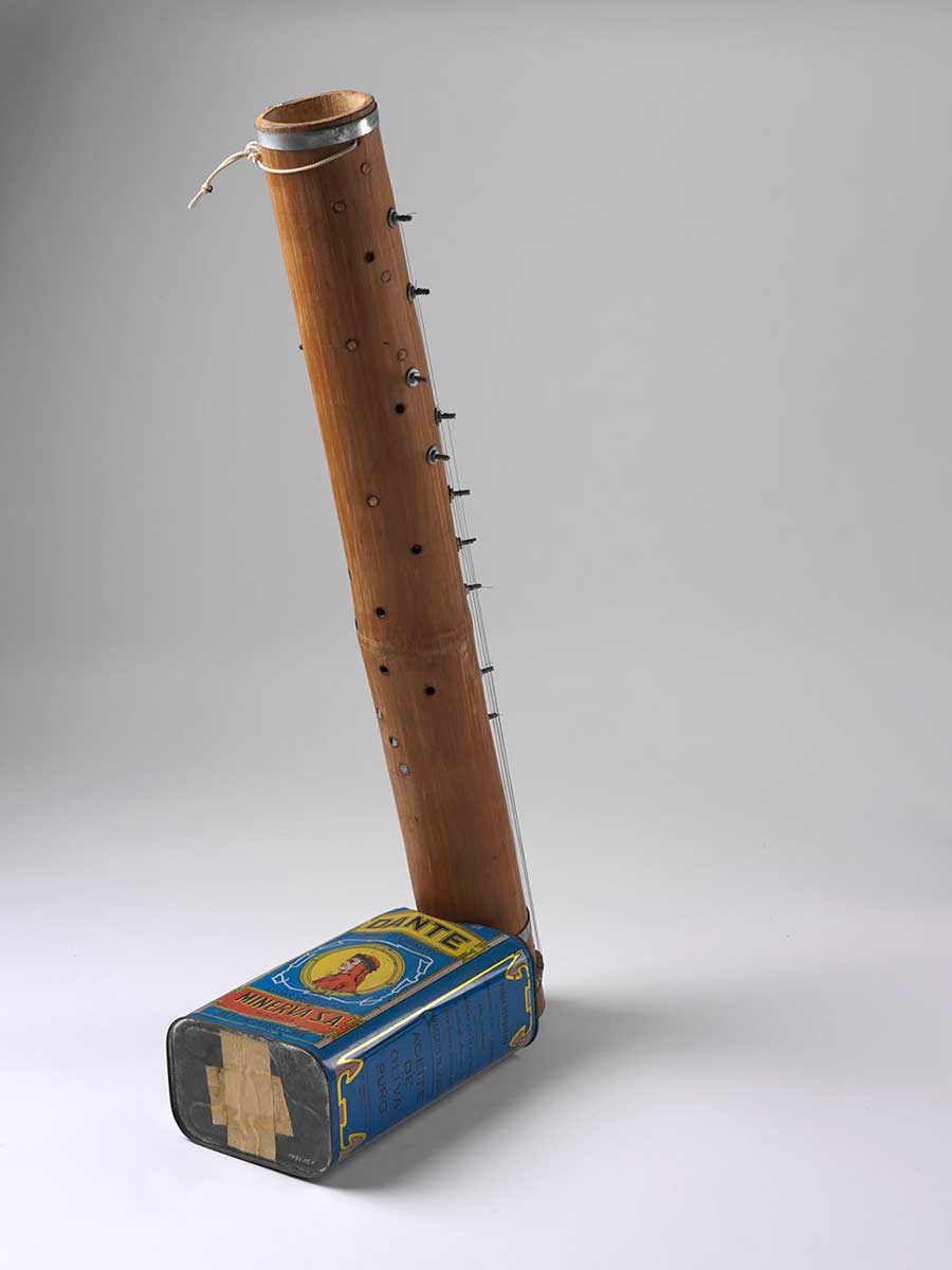 A musical instrument consisting of a bamboo tube with keys and strings down the sides and a blue olive oil tin at the base. - click to view larger image