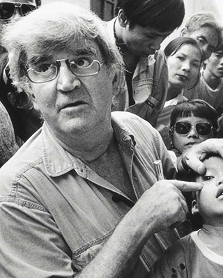 Fred Hollows points to the left eye of a young boy at a busy clinic in Vietnam. - click to view larger image